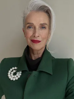 Maureen Pike, silver hair swept up, red lipstick, green coat with a pearl brooch.