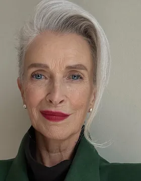 Maureen Pike, head and shoulders, silver hair swept back, red lipstick, pearl stud earrings.