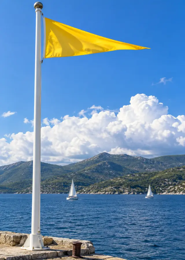 A yellow pennant streaming from a white flagpole, clouds building over the hills.