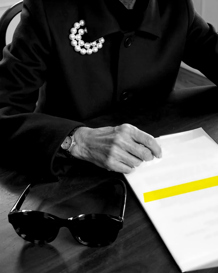 Maureen Pike, an AI character: her hand rests on a page of small print, one line marked with yellow highlighter, her folded sunglasses beside it.