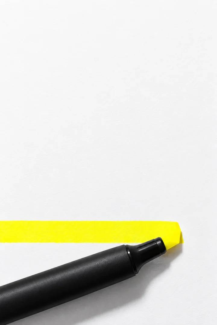 A black highlighter pen resting at the end of a single bright yellow stroke across blank white paper.